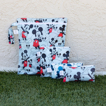 Four waterproof Bumkins Wet Bag: Mickey Mouse Classic zippered bags on grass, featuring colorful character prints in various sizes.