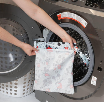 Someone is putting a Bumkins Wet Bag: Mickey Mouse Classic, made with waterproof fabric, into a front-loading washing machine.