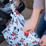 A person holds a Bumkins Wet Bag: Mickey Mouse Classic, next to a child in a stroller with a charming Bumkins SuperBib.