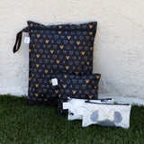 Four Bumkins Minnie Mouse Icon Black + White zippered wet bags are on grass against a textured wall. They boast waterproof fabric, hearts, and bows.