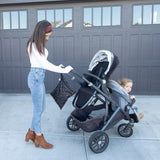 Woman in a white top pushes a stroller by the garage, carrying a Bumkins Minnie Mouse Icon Black + White wet bag.