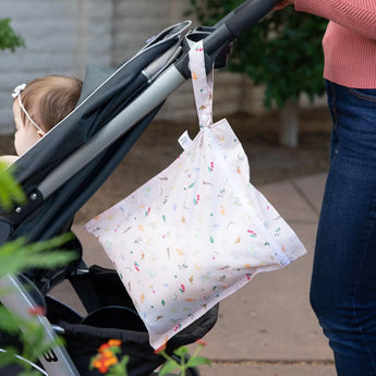 A toddlers stroller handle stylishly holds a reusable, waterproof Bumkins Wet Bag: Princess Magic.