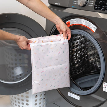 A person puts a Bumkins Princess Magic Wet Bag into a front-load washing machine.