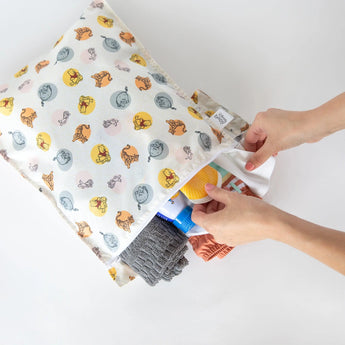 Hands organizing items in the Bumkins Wet Bag: Winnie and Friends. Perfect reusable pouch for clothes and bottles.