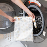 Person placing a Bumkins Wet Bag: Winnie and Friends into a front-loading washing machine.