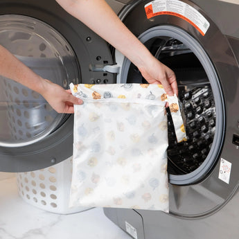 Person placing a Bumkins Wet Bag: Winnie and Friends into a front-loading washing machine.