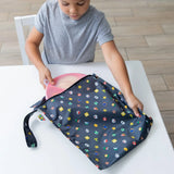 Child placing a pink plate into the Bumkins Wet Bag: Super Mario™ Lineup, made of waterproof fabric, at a white table.