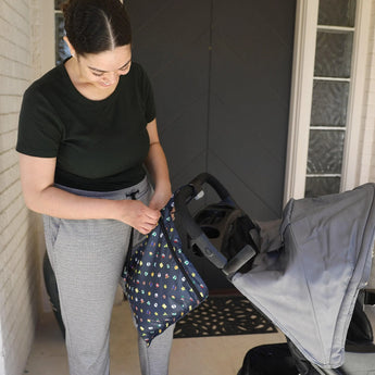 Woman in green adjusts a Bumkins Wet Bag: Super Mario™ Lineup on stroller outside door.