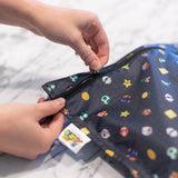 Hands zipping the Bumkins Wet Bag: Super Mario™ Lineup with vibrant graphics, made of waterproof fabric, on a marble surface.