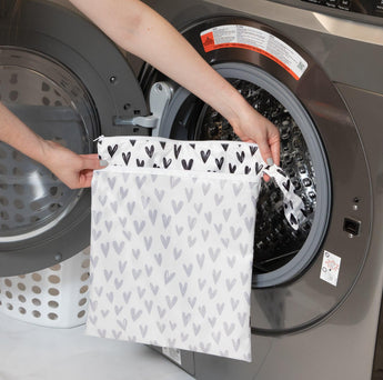 Person puts a Bumkins Wet/Dry Bag: Hearts, with waterproof protection, into a front-loading washing machine.