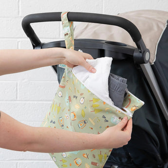 Person adding items to a Bumkins Wet/Dry Bag: Camp Gear made of waterproof fabric attached to a strollers handle.