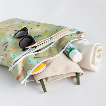 Bumkins Wet/Dry Bag: Camp Gear with sunglasses, towel & sunscreen peeking out against a white background. Waterproof & stylish pattern.