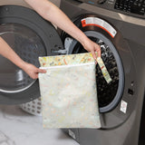 Person holding a Bumkins Wet/Dry Bag: Camp Gear in front of an open washing machine, ideal for travel organization.