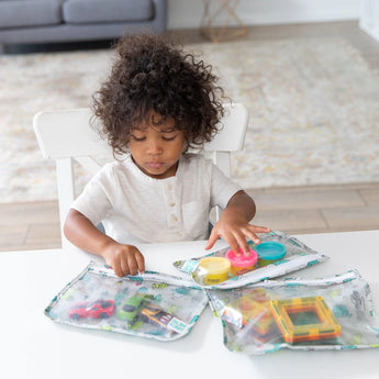 Child at table playing with toys next to Bumkins Clear Travel Bag 3-Pack: Cacti, three TSA compliant, reusable bags.