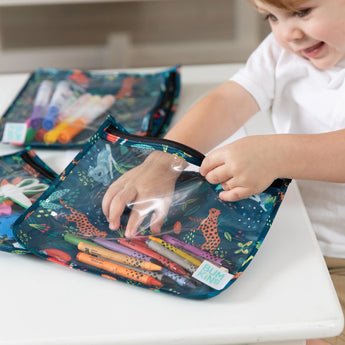 A child smiles organizing markers in a Bumkins Clear Travel Bag, Jungle theme, perfect for TSA-compliant travel needs.