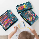 A child draws with crayons surrounded by Bumkins Clear Travel Bag 3-Pack: Jungle, filled with colored pencils and markers.