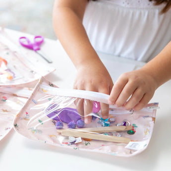 A child expertly packs craft supplies into the TSA-compliant Bumkins Princess Magic Clear Travel Bag, part of a 3 pack.