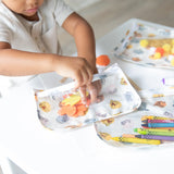 A child crafts joyfully at the table with colorful supplies in a Bumkins Clear Travel Bag: Winnie and Friends set.