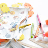 Colorful pencils and crayons near a Bumkins Clear Travel Bag with Winnie and Friends stickers.