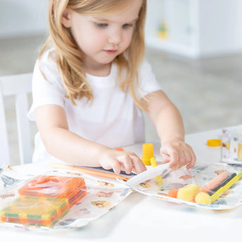 A child in a white shirt explores colorful toys and art supplies, imagining adventures with the Bumkins Winnie and Friends Travel Bag.