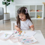 A young girl colors with crayons while Bumkins Clear Travel Bag 3-Pack: Lace sits on a nearby white shelf.