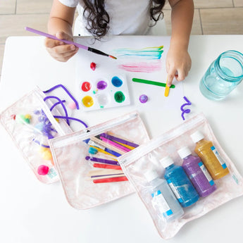 Child painting with colorful paints, using Bumkins Clear Travel Bag 3-Pack to keep art supplies organized and TSA compliant.