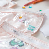 Close-up of Bumkins Clear Travel Bag 3-Pack: Lace with playful designs on a table, surrounded by colorful stickers and crayons.