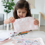 A young girl plays with craft items, her pink fabric neatly stored in Bumkins Clear Travel Bag 3-Pack: Lace.